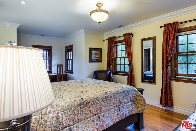 bedroom featuring multiple windows, crown molding, and light wood-type flooring