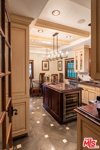 bar with hanging light fixtures, sink, cream cabinets, ornamental molding, and beverage cooler