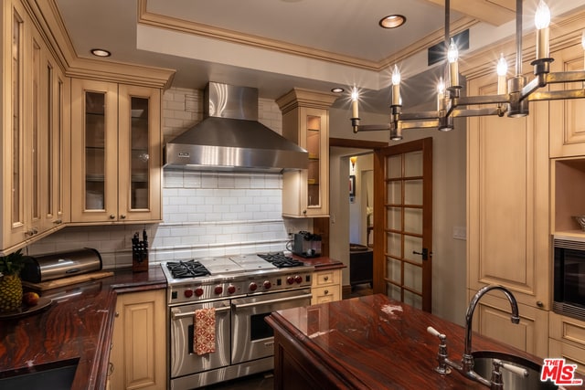 kitchen featuring appliances with stainless steel finishes, decorative backsplash, wall chimney range hood, sink, and pendant lighting