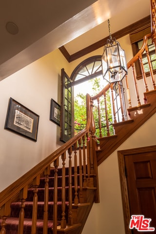 stairs featuring crown molding and an inviting chandelier