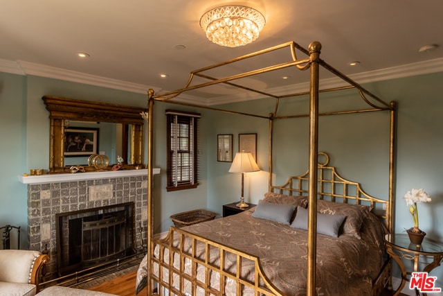 bedroom featuring crown molding, a tiled fireplace, and wood-type flooring