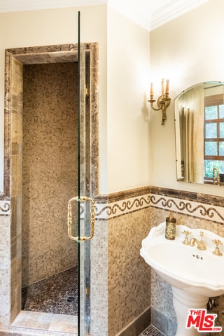 bathroom with tile walls, a shower with door, and crown molding