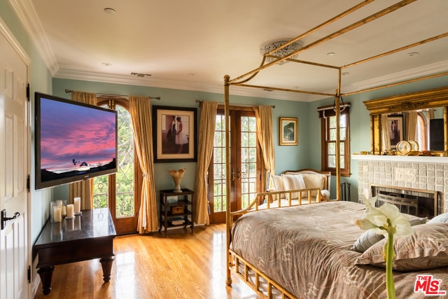 bedroom featuring a brick fireplace, crown molding, and french doors