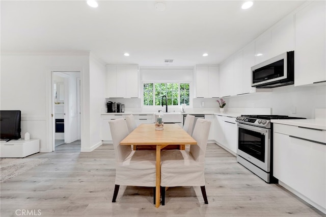 kitchen with appliances with stainless steel finishes, sink, white cabinets, ornamental molding, and light hardwood / wood-style floors