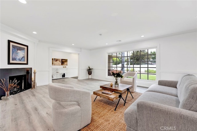 living room featuring ornamental molding, light hardwood / wood-style flooring, and a tiled fireplace