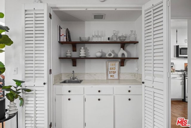 bar with sink, white cabinetry, appliances with stainless steel finishes, and parquet floors