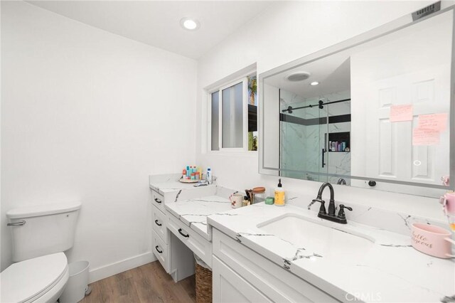 bathroom featuring hardwood / wood-style flooring, toilet, a shower with shower door, and vanity