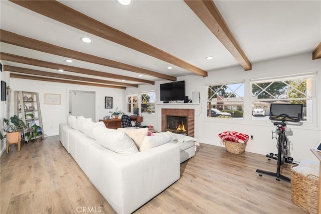 living room with light hardwood / wood-style flooring, beamed ceiling, and a brick fireplace