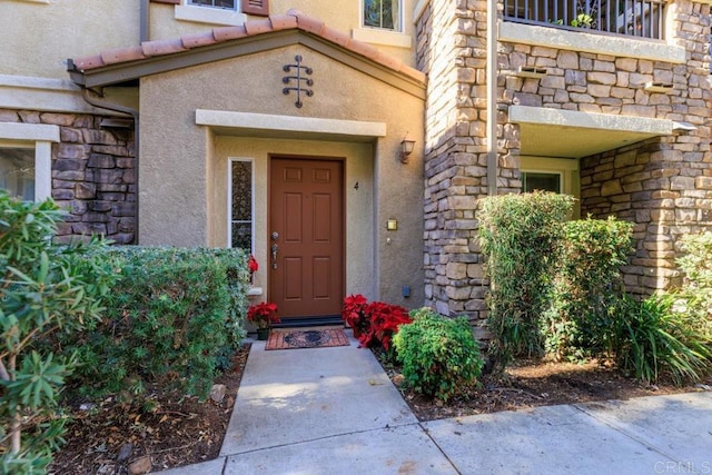 property entrance with stone siding, a tiled roof, and stucco siding