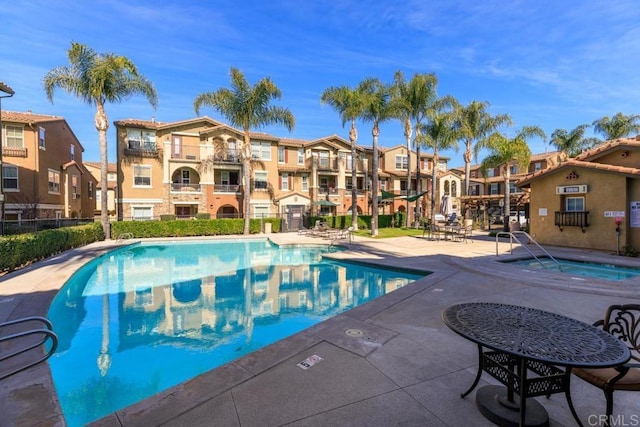 pool featuring a patio, a community hot tub, fence, and a residential view