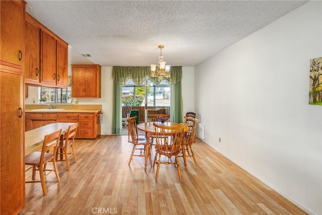 dining area featuring a notable chandelier, light wood-type flooring, a textured ceiling, and sink