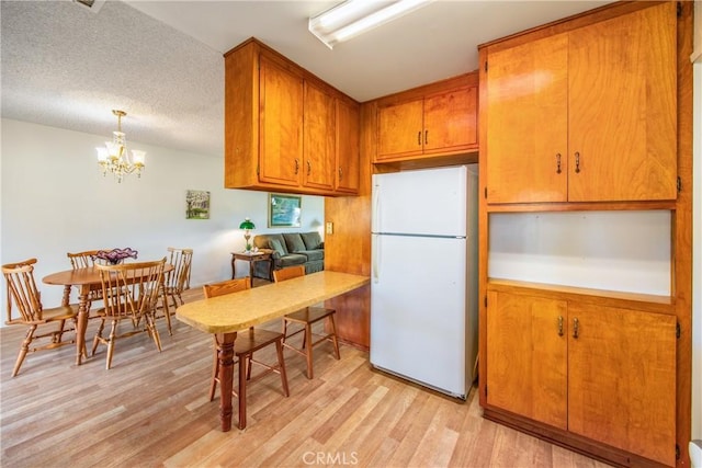 kitchen with light hardwood / wood-style floors, a textured ceiling, hanging light fixtures, white fridge, and an inviting chandelier