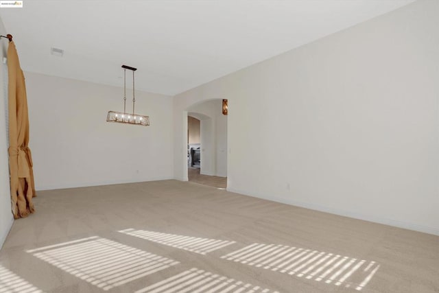 unfurnished room with light colored carpet and an inviting chandelier