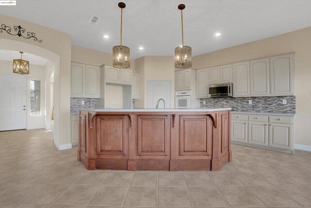 kitchen with white cabinets, a kitchen island with sink, white oven, and hanging light fixtures