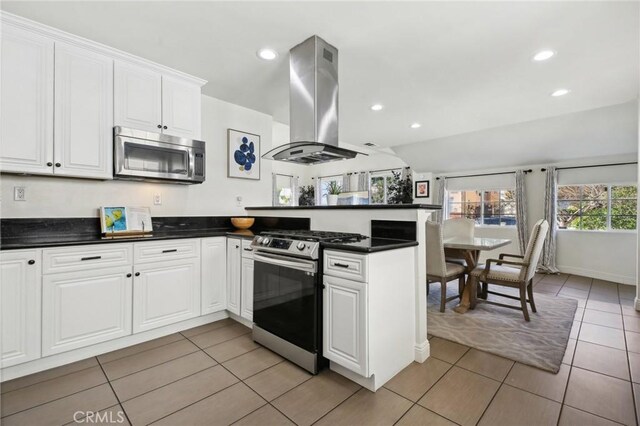 kitchen featuring a peninsula, island exhaust hood, white cabinets, appliances with stainless steel finishes, and dark countertops