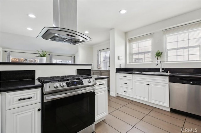 kitchen with island exhaust hood, a sink, appliances with stainless steel finishes, white cabinetry, and dark countertops