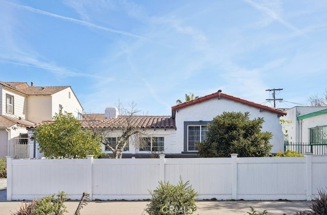 view of front facade featuring a tiled roof, fence, and stucco siding