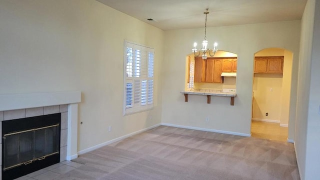 unfurnished living room with a tiled fireplace, light carpet, and a notable chandelier