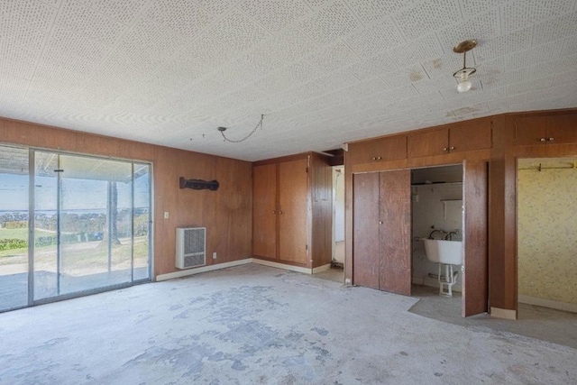 unfurnished bedroom featuring sink, heating unit, wood walls, and access to outside