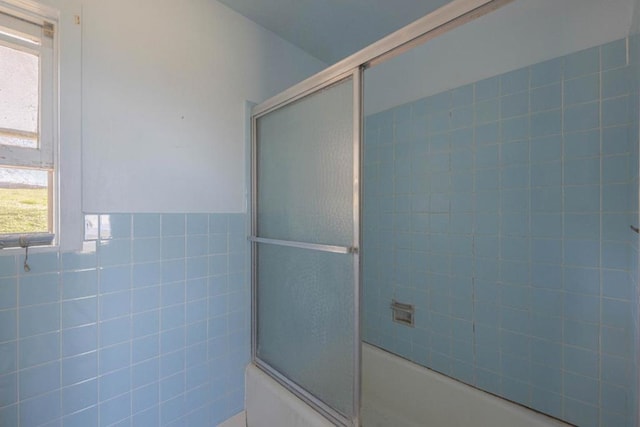 bathroom with plenty of natural light, bath / shower combo with glass door, and tile walls