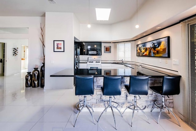 kitchen featuring a skylight, white gas range, sink, light tile patterned floors, and kitchen peninsula