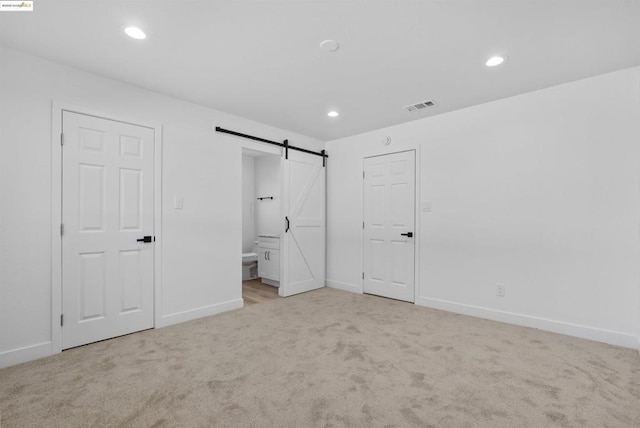 unfurnished bedroom with light carpet, a barn door, and ensuite bathroom