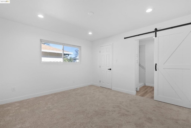 unfurnished bedroom with a closet, light colored carpet, and a barn door