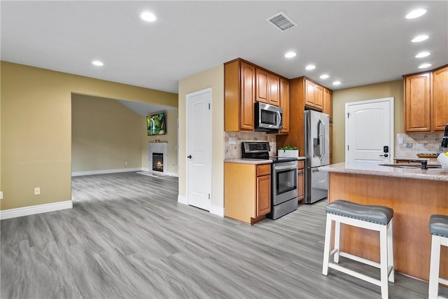 kitchen featuring tasteful backsplash, appliances with stainless steel finishes, light wood-type flooring, and a kitchen bar