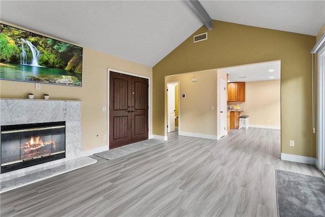 unfurnished living room with vaulted ceiling with beams, a fireplace, and light hardwood / wood-style floors