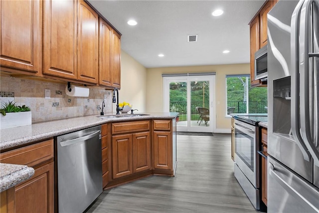 kitchen with appliances with stainless steel finishes, sink, backsplash, light stone countertops, and light hardwood / wood-style flooring