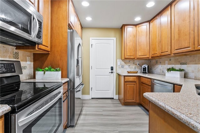 kitchen featuring light stone counters, tasteful backsplash, light hardwood / wood-style floors, and appliances with stainless steel finishes