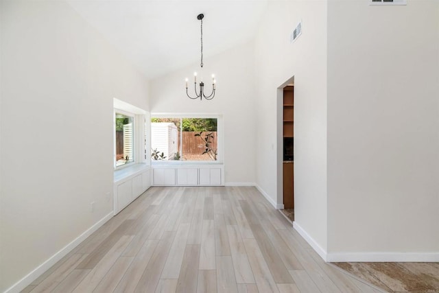 unfurnished dining area with light hardwood / wood-style floors, high vaulted ceiling, and a notable chandelier