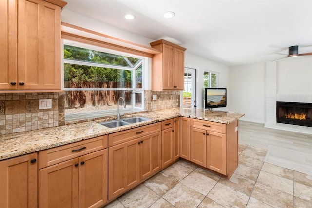 kitchen featuring a fireplace, sink, decorative backsplash, light stone counters, and kitchen peninsula