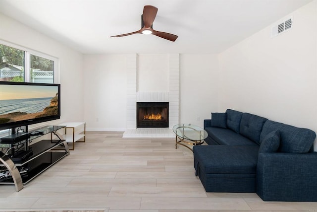 living room featuring ceiling fan, a brick fireplace, and light hardwood / wood-style floors