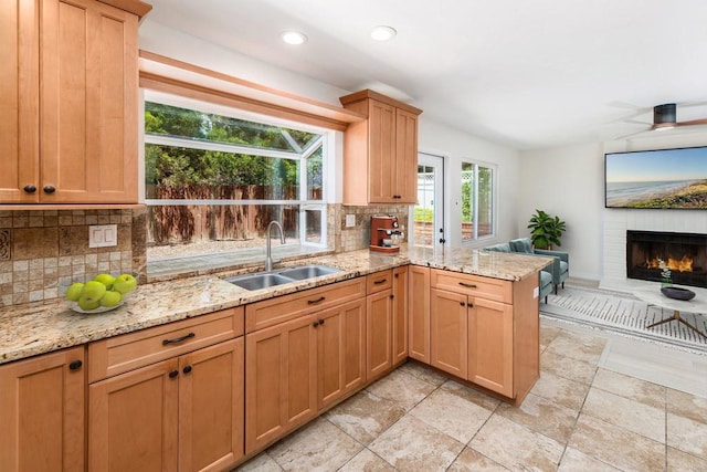 kitchen with sink, light stone counters, tasteful backsplash, a brick fireplace, and kitchen peninsula