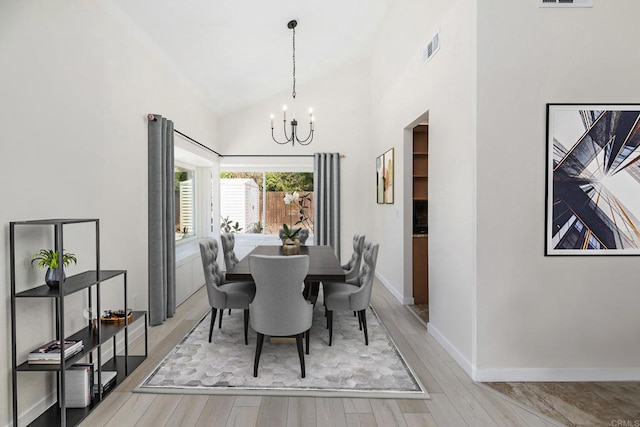 dining area featuring a notable chandelier, light hardwood / wood-style flooring, and high vaulted ceiling