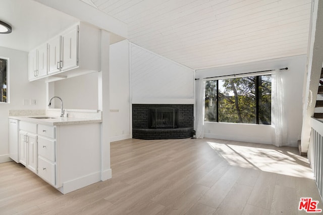 unfurnished living room featuring sink, light wood-type flooring, wooden ceiling, and a fireplace