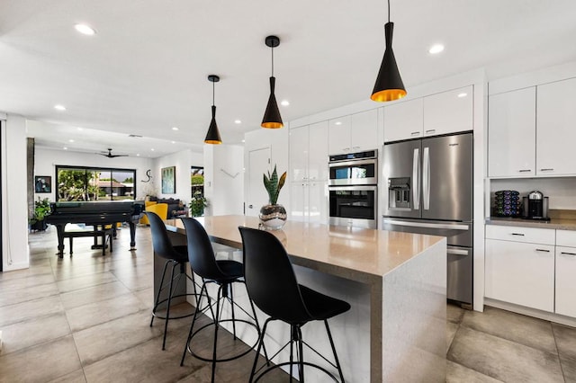 kitchen with pendant lighting, a breakfast bar area, ceiling fan, stainless steel appliances, and white cabinets