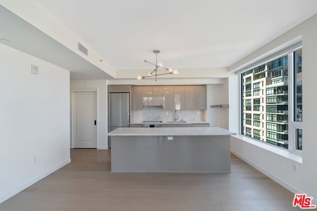 kitchen with light hardwood / wood-style flooring, stainless steel built in refrigerator, sink, tasteful backsplash, and a notable chandelier