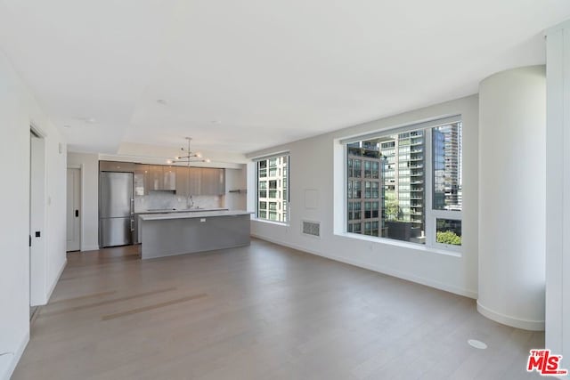 unfurnished living room with sink, a chandelier, and light hardwood / wood-style flooring