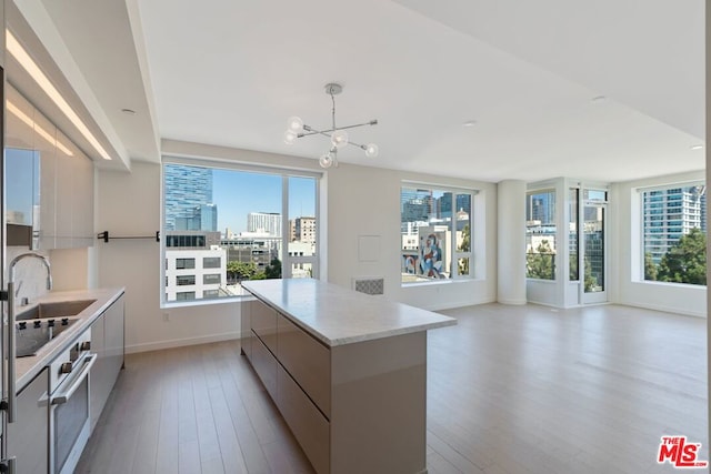 kitchen featuring a spacious island, pendant lighting, sink, oven, and light hardwood / wood-style flooring