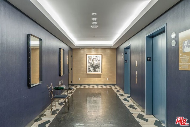 hallway with elevator and a raised ceiling