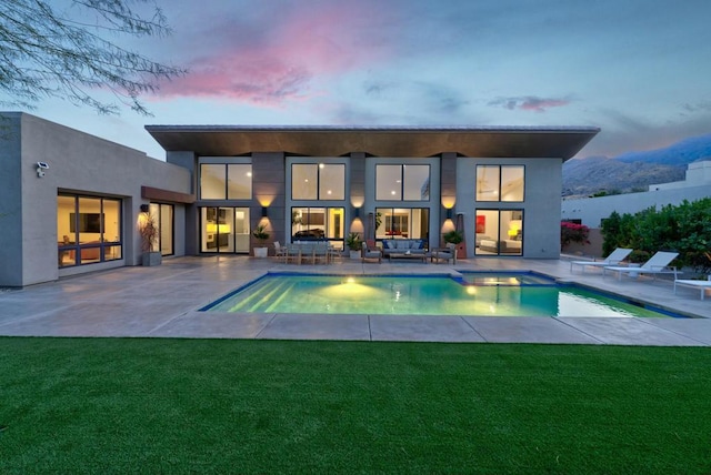 back house at dusk with a lawn and a patio