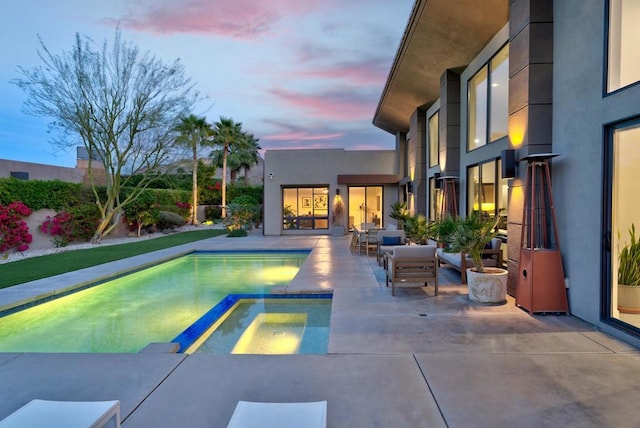 pool at dusk featuring an in ground hot tub and a patio