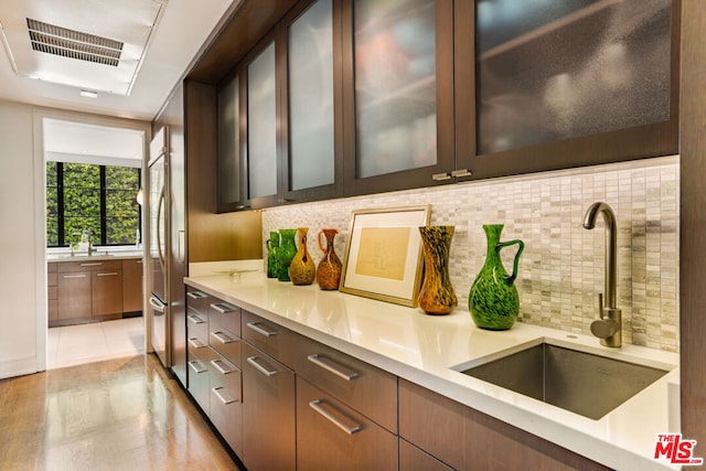 bar with sink, high quality fridge, dark brown cabinets, and tasteful backsplash