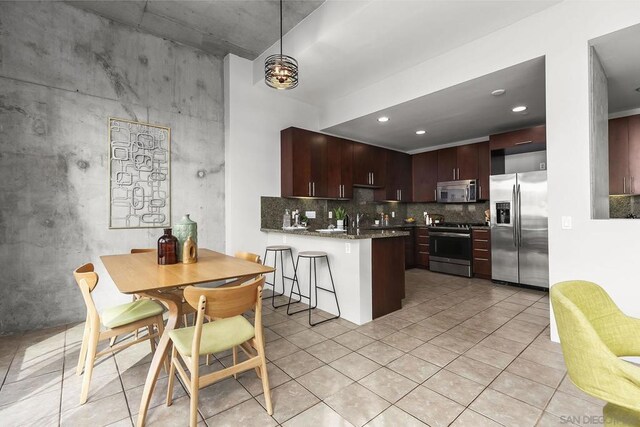 kitchen with dark brown cabinetry, stainless steel appliances, backsplash, kitchen peninsula, and light tile patterned floors