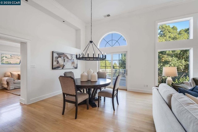 dining space with light hardwood / wood-style floors, a towering ceiling, crown molding, and a notable chandelier