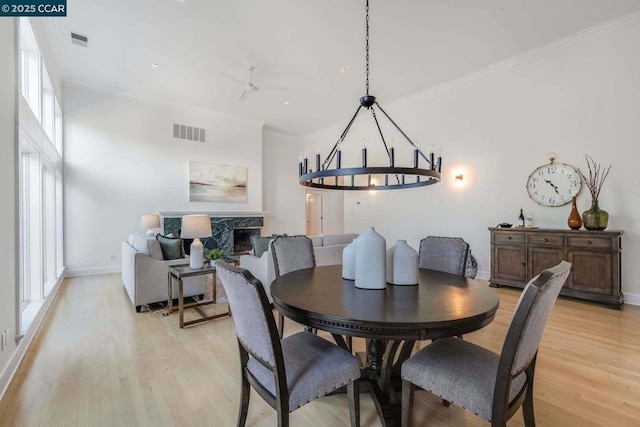 dining room featuring light wood-type flooring, a wealth of natural light, a high end fireplace, and crown molding