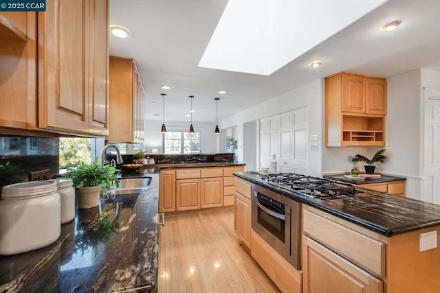 kitchen featuring appliances with stainless steel finishes, decorative light fixtures, sink, a skylight, and dark stone countertops