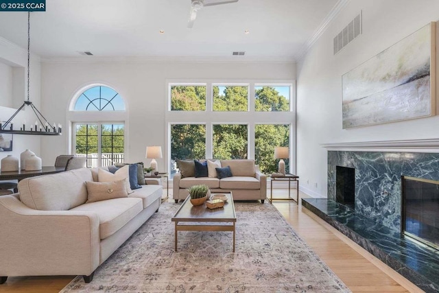 living room featuring light wood-type flooring, a towering ceiling, a premium fireplace, and ornamental molding